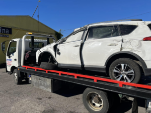 A heavily damaged white SUV being towed on a flatbed truck by Anytime towing services in Columbus, OH.