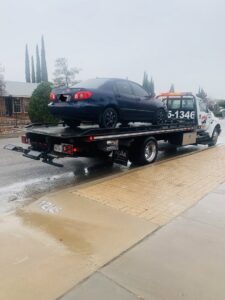 A dark blue sedan being transported on a flatbed tow truck by Tow-Ro Towing in El Paso, TX.