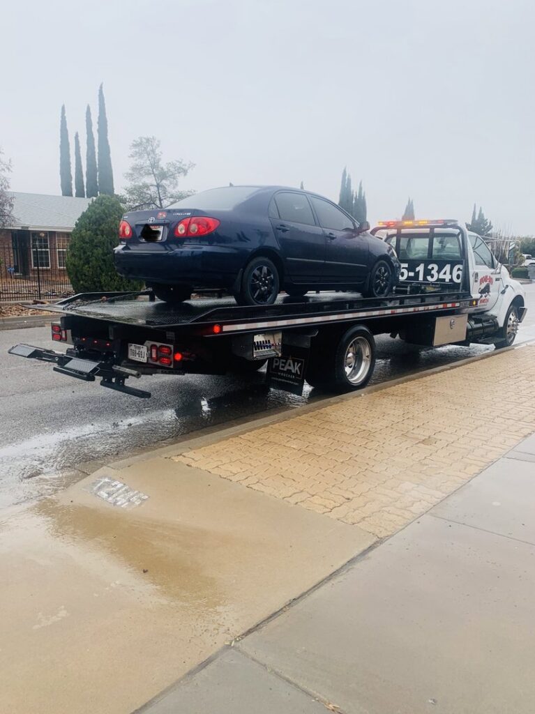 A dark blue sedan being transported on a flatbed tow truck by Tow-Ro Towing in El Paso, TX.