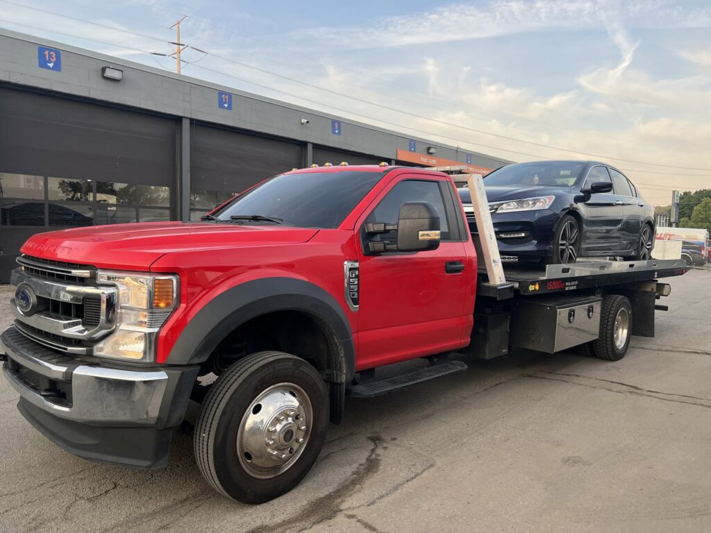 A dark blue sedan being transported on a flatbed tow truck by Quiñones Towing in Cleveland, OH.
