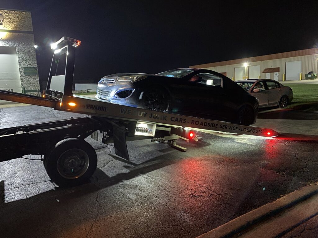 A dark blue sports car being loaded onto a flatbed tow truck at night by Towing Recovery Rebuilding Assistance Services in Naperville, IL