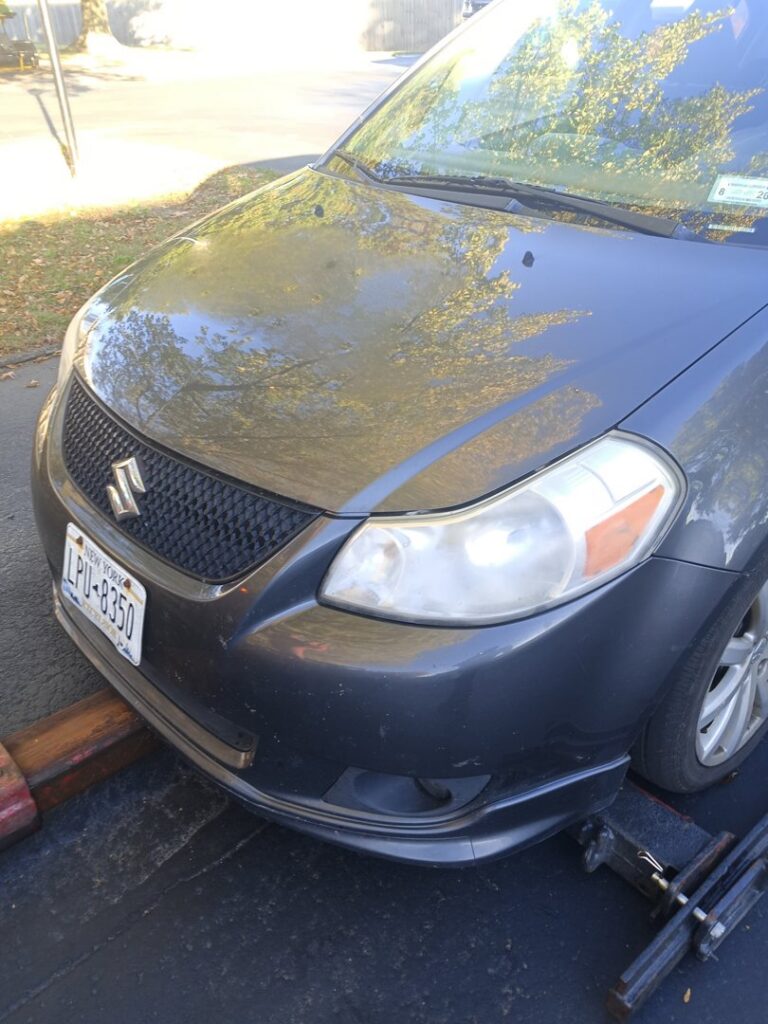 A dark gray car with its front wheels secured on a tow dolly, ready for transport by Buffalo Towing Services in Buffalo, NY.