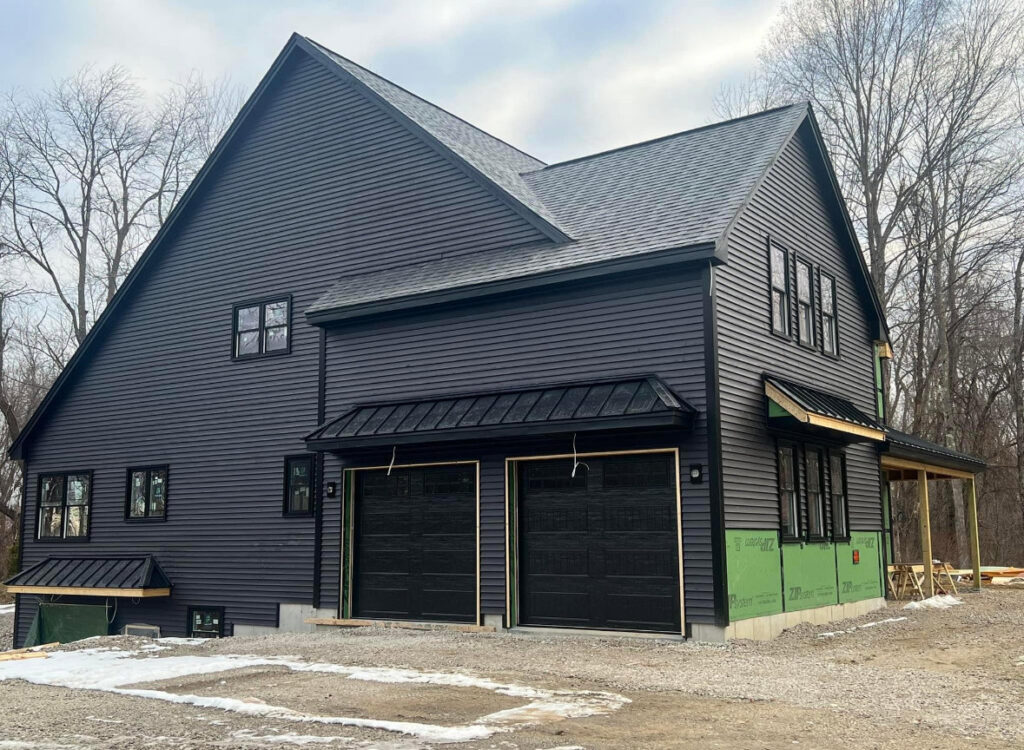 A dark gray modern house featuring two black panel garage doors, a completed project by Steve Shumsky Unlimited Overhead Doors LLC in Hudson, NH