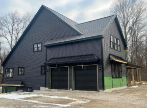 A dark gray modern house featuring two black panel garage doors, a completed project by Steve Shumsky Unlimited Overhead Doors LLC in Hudson, NH