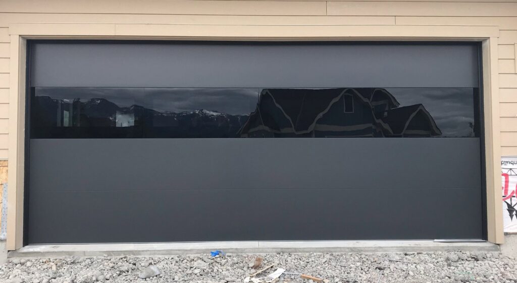 A dark gray modern garage door with a reflective horizontal window strip, installed by Riverside Garage Doors in Kalispell, MT.