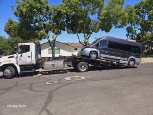 A dark grey camper van being towed on a flatbed tow truck by Ibanez Towing Service LLC in San Jose, CA.