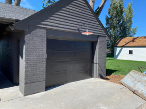 A modern dark grey garage door installed on a brick garage by MBP Garage Doors in Firth, ID