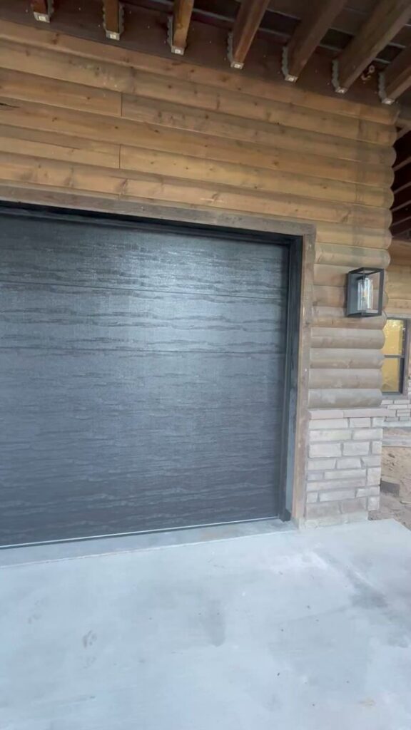 A dark grey garage door installed on a rustic log cabin style building by Barrett Overhead Doors in Idaho Falls, ID.