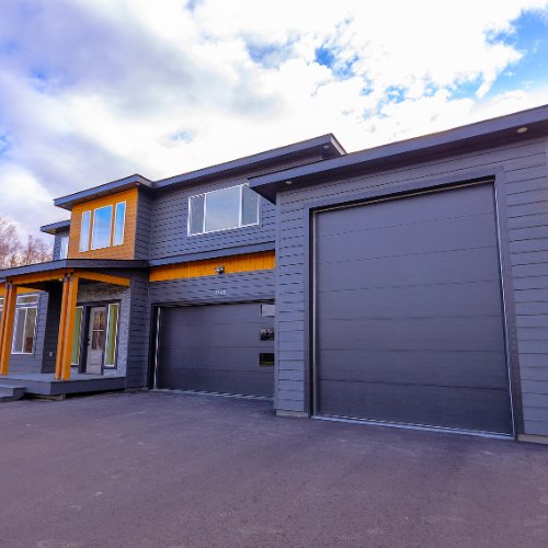 Two dark grey garage doors with small windows installed on a modern residential property by Elite Doors in Wasilla, AK.