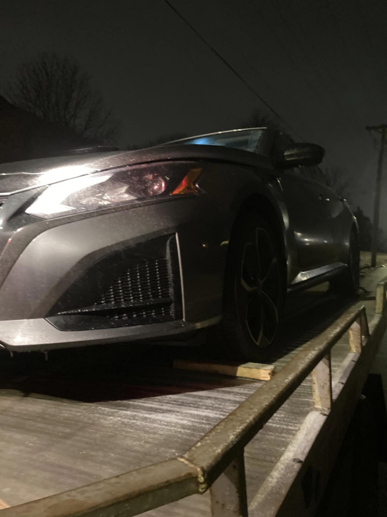 A dark grey sedan loaded onto a flatbed tow truck at night by FSC INC in Omaha, NE.