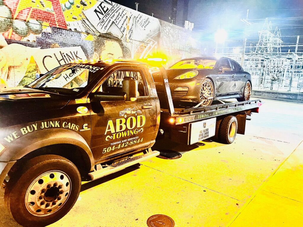 A dark Porsche being towed on a flatbed truck by ABOD Towing LLC in New Orleans, LA, at night.