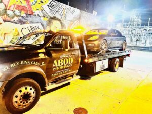 A dark Porsche being towed on a flatbed truck by ABOD Towing LLC in New Orleans, LA, at night.