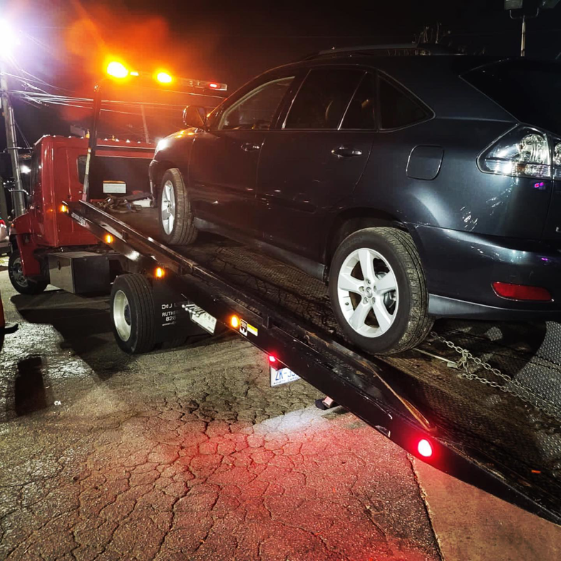 A dark SUV being loaded onto a red flatbed tow truck by RDU Towing & Recovery Services in Raleigh, NC.