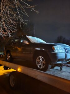 A dark SUV being towed on a flatbed tow truck at night by Luck's Unlimited Towing in Thornton, CO.
