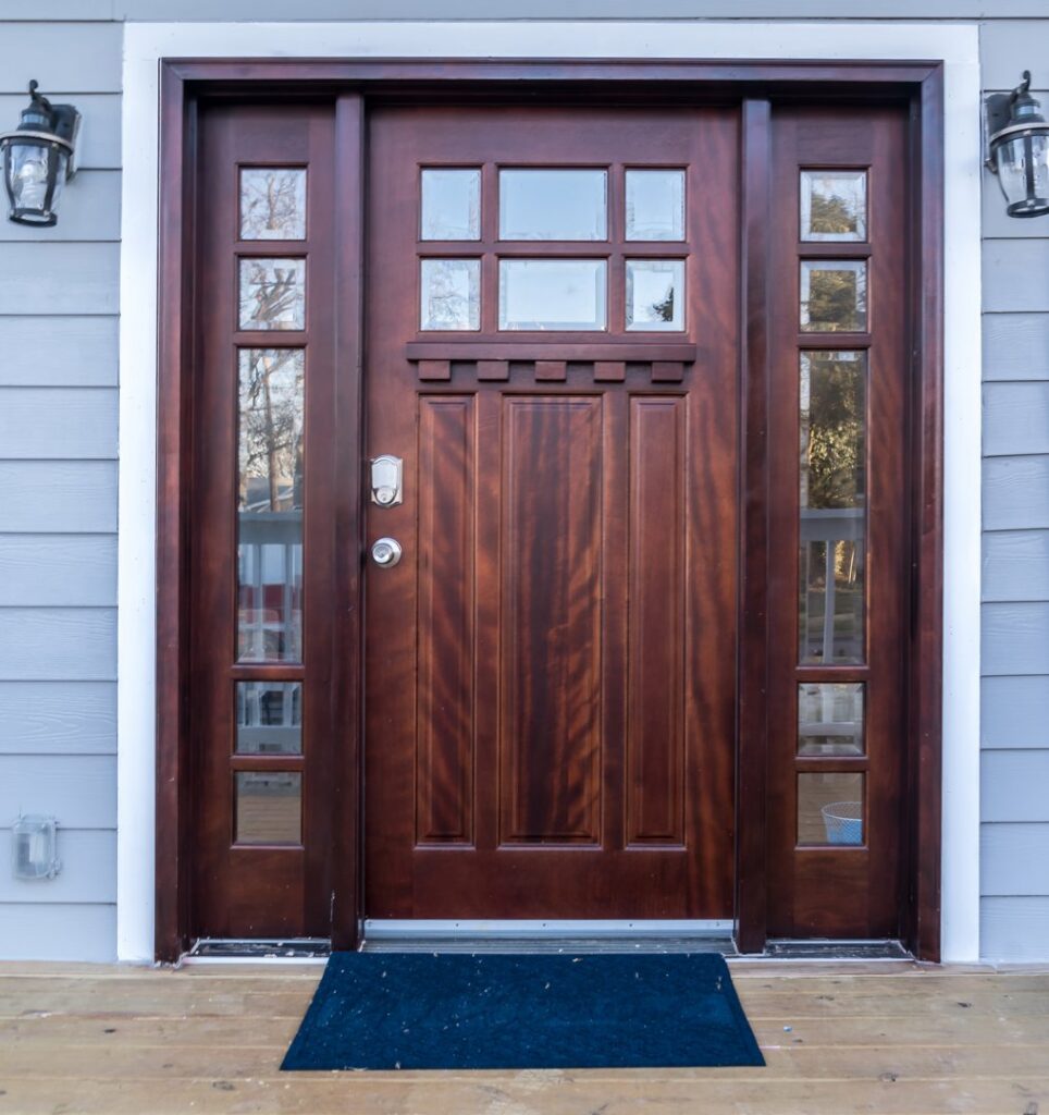 A dark wood front door with glass panels, complemented by light blue horizontal siding on a house, by Jonesboro Siding, Window & Door in Jonesboro, AR.