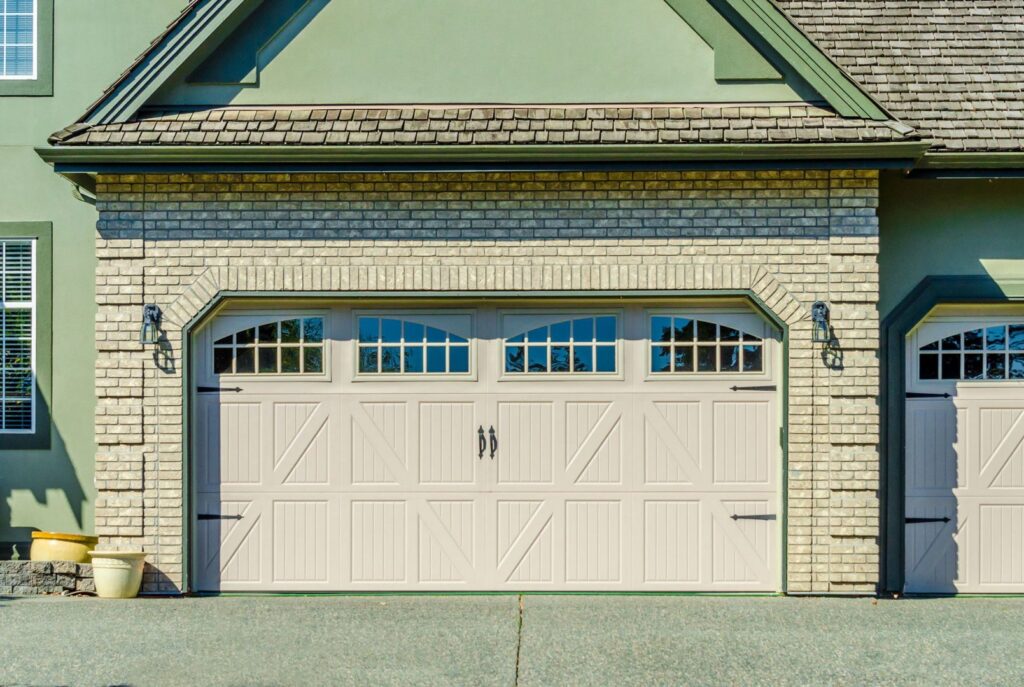 A decorative beige garage door with windows and hardware on a brick house by PS Garage Doors of Williston, ND.