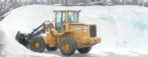 A yellow Deere front-end loader next to a large pile of salt, used for de-icing by Total Lot Maintenance in St. Charles, MO.