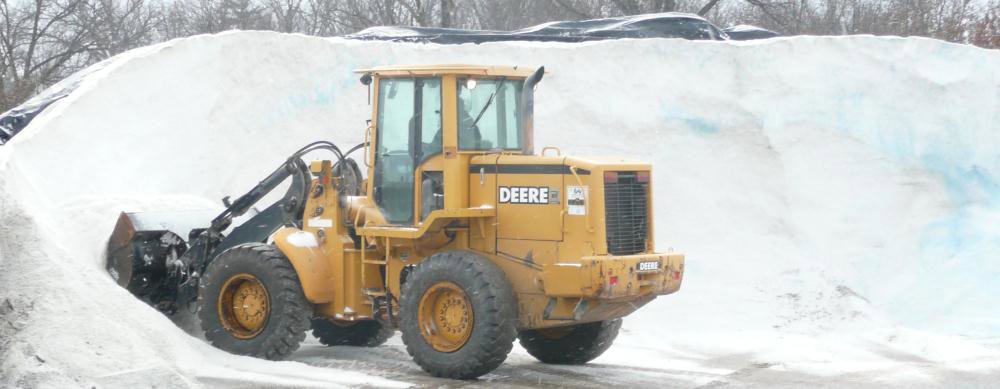 A yellow Deere front-end loader next to a large pile of salt, used for de-icing by Total Lot Maintenance in St. Charles, MO.