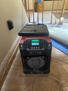A powerful dehumidifier drying a water-damaged carpet and subfloor during restoration by Elements of Restoration in Denver, CO.