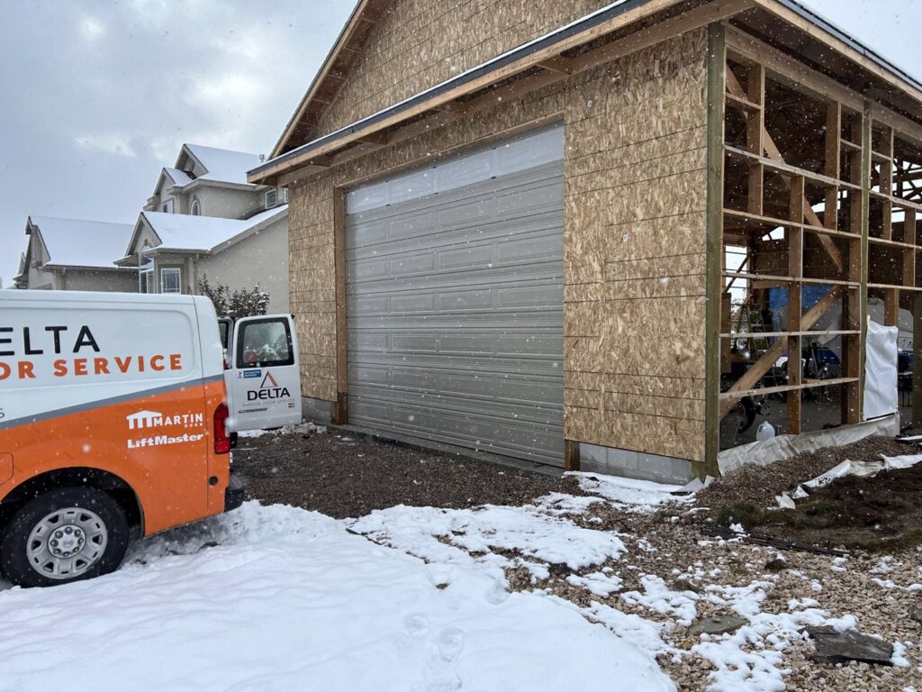 A Delta Garage Door service van parked next to a garage door on a snowy day, providing service in Millcreek, UT.
