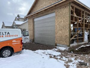 A Delta Garage Door service van parked next to a garage door on a snowy day, providing service in Millcreek, UT.
