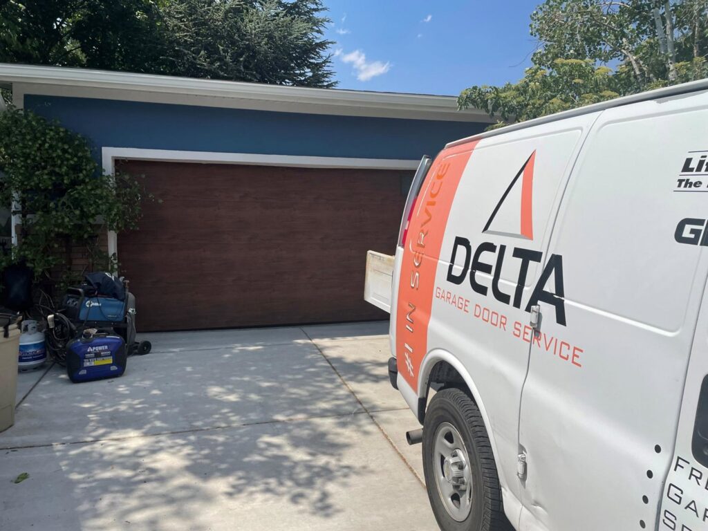 A Delta Garage Door service van parked in front of a house with a brown garage door, indicating on-site service in Millcreek, UT.