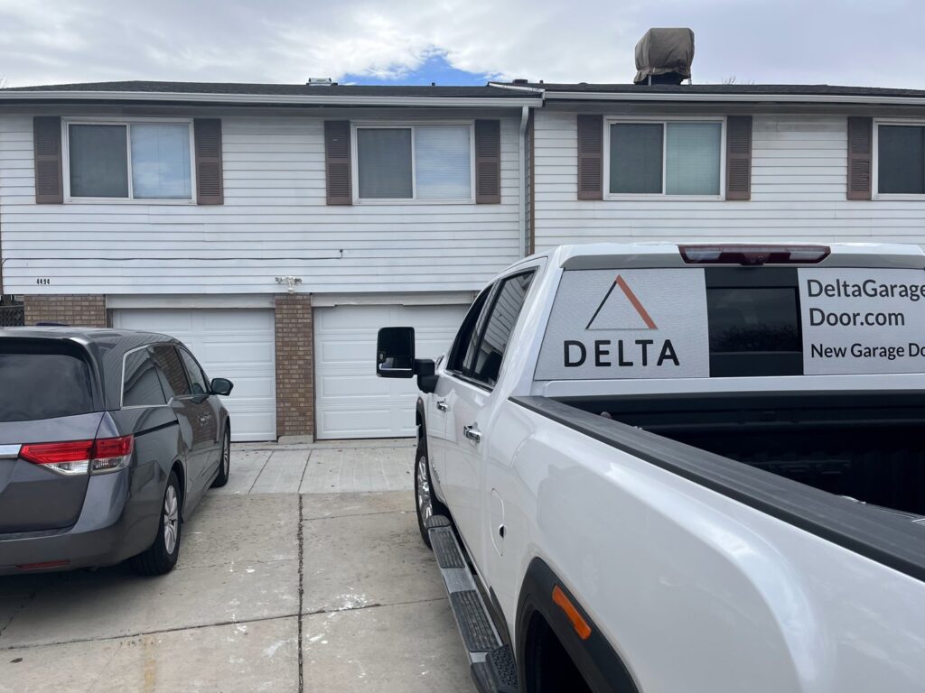 A Delta Garage Door branded truck parked in front of two white garage doors, ready for service in Millcreek, UT.