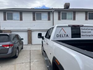 A Delta Garage Door branded truck parked in front of two white garage doors, ready for service in Millcreek, UT.