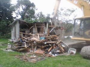 A large pile of debris from a demolished house, with an excavator nearby, by Dade Wrecking Demolition LLC in Miami, FL.