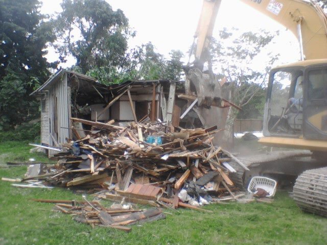 A large pile of debris from a demolished house, with an excavator nearby, by Dade Wrecking Demolition LLC in Miami, FL.