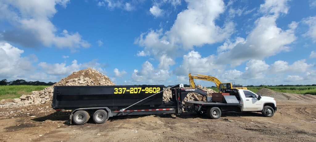 A dump trailer filled with demolition debris, with an excavator loading more material for Judice Dirt & Demolition in Lafayette, LA.