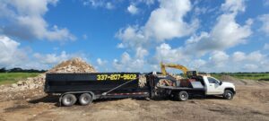 A dump trailer filled with demolition debris, with an excavator loading more material for Judice Dirt & Demolition in Lafayette, LA.