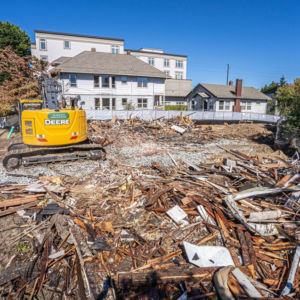 An excavator on a demolition site with a large pile of debris, showing cleanup by Rainstate Earthworks in Auburn, WA.