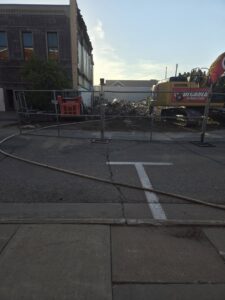 A demolition site with an excavator from DeCarlo Demolition Company visible from the street in Des Moines, IA.