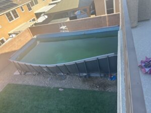 A neglected above-ground pool with very green, dirty water, requiring professional cleaning from Overflow Poolz LLC in Las Vegas, NV.