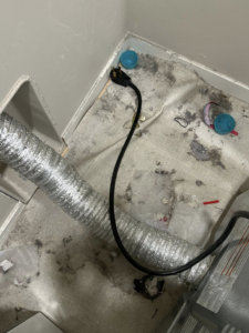 A very dirty area behind a dryer with lint and dust, showing a deep cleaning service by E & S Cleaning Services L.L.C in Nampa, ID.