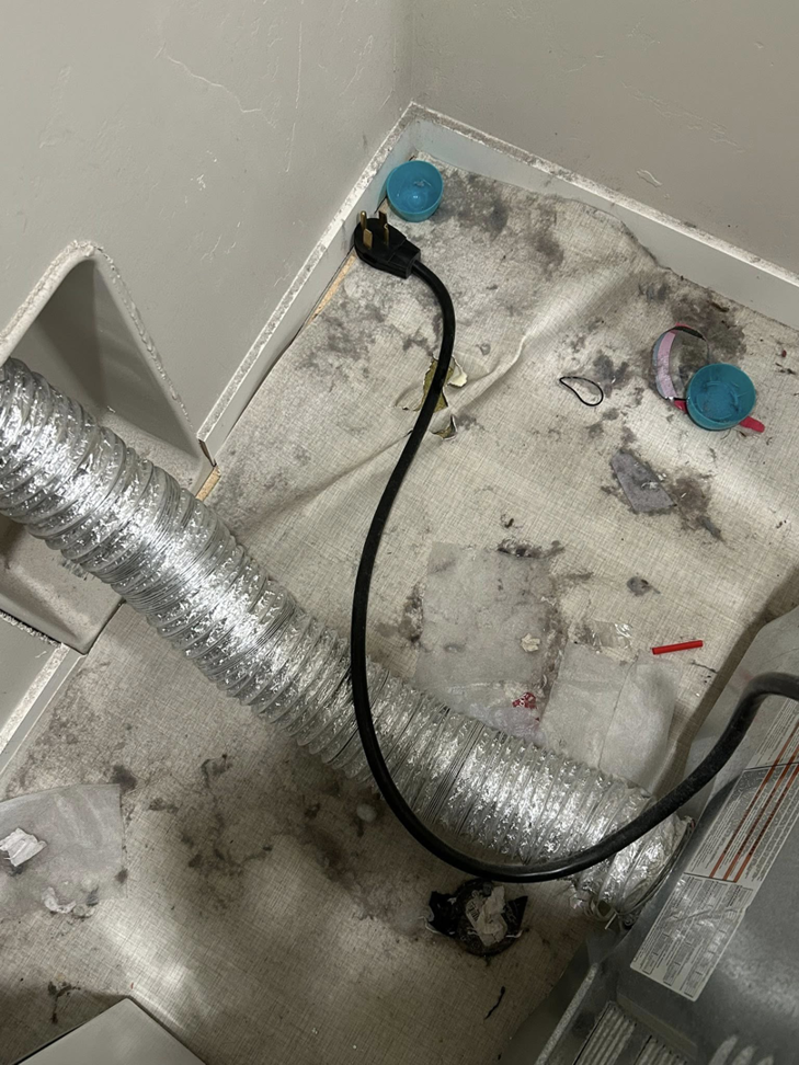 A very dirty area behind a dryer with lint and dust, showing a deep cleaning service by E & S Cleaning Services L.L.C in Nampa, ID.