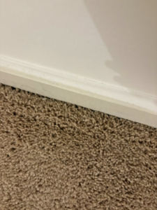 A dirty baseboard above a carpeted floor, ready for cleaning by Danielle's cleaning service in Xenia, OH
