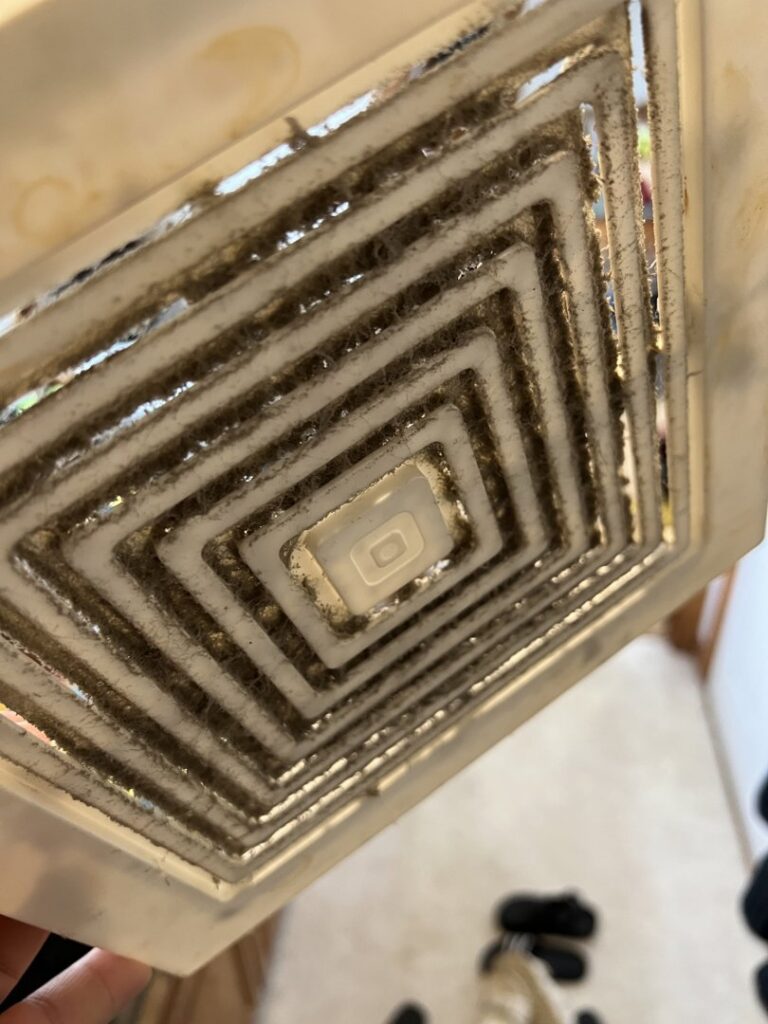 An extremely dirty bathroom exhaust fan cover caked with dust and grime, highlighting a deep cleaning service offered by Little Cubs Cleaning Services in Rochester, MN.