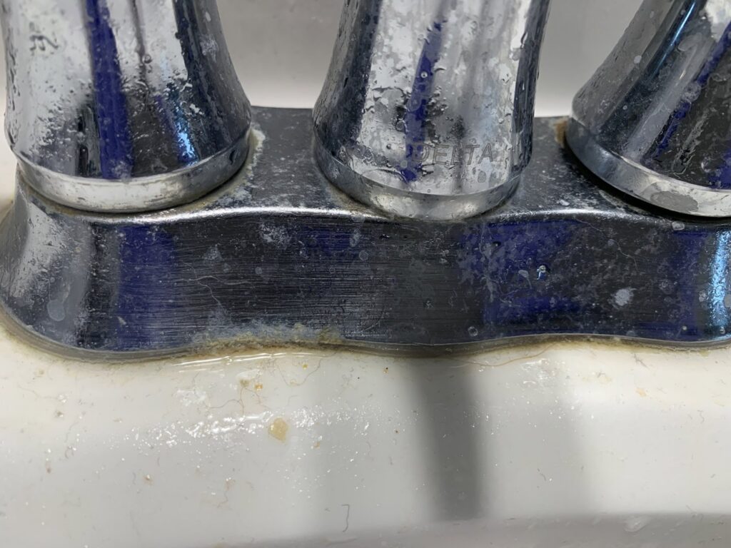 A dirty bathroom faucet base with hard water stains and grime before professional cleaning by Cuse Cleaning in Syracuse, NY.