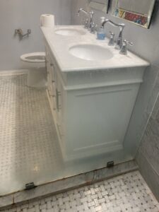 Dirty bathroom vanity with two sinks and glass shower door showing water spots, for cleaning by Jolley Services, INC in Bossier City, LA.