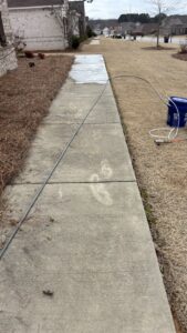 A dirty concrete pathway with a hose running along it, before washing by Plains Power Washing in Auburn, AL.