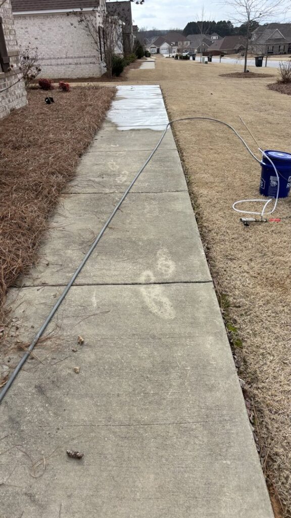 A dirty concrete pathway with a hose running along it, before washing by Plains Power Washing in Auburn, AL.