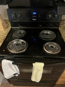 A dirty black electric stove and oven before cleaning, showing grime on the stovetop, by You have it maid in Canton, MI.