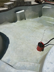 A dirty, empty swimming pool with a cleaning vacuum from Stephens Pool Service in Oklahoma City, OK.
