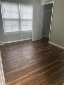 A dirty and empty room with dull wood floors before professional residential cleaning by VM Residential cleaning LLC in Baton Rouge, LA.