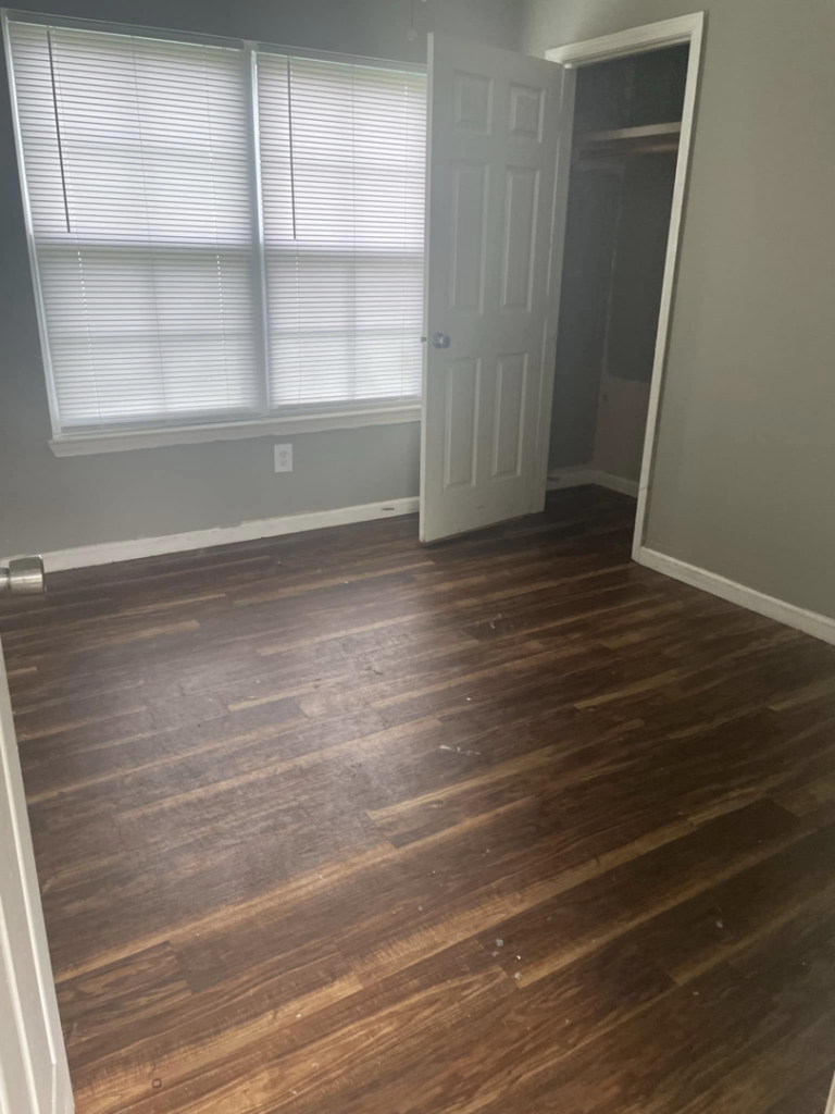A dirty and empty room with dull wood floors before professional residential cleaning by VM Residential cleaning LLC in Baton Rouge, LA.