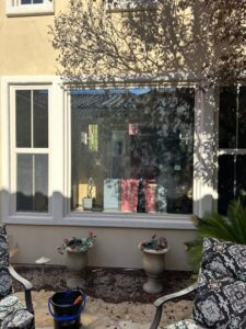 A dirty exterior window with a cleaning bucket and tools nearby, ready for professional window cleaning by JG Clean Solutions in Henderson, NV.