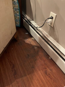 A dirty floor and baseboard with debris, showing an area before cleaning by Straight Up Cleaning in South Portland, ME.