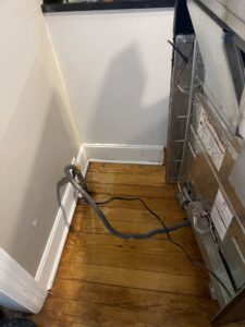 A dirty floor area with debris and wires behind an appliance, showing a space needing deep cleaning by JLJ Sister's Cleaning & More in Lexington, KY.